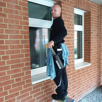 ein Mitarbeiter von Neesen Glas- und Innenreinigung putzt ein Fenster mit einem Abzieher und Lappen